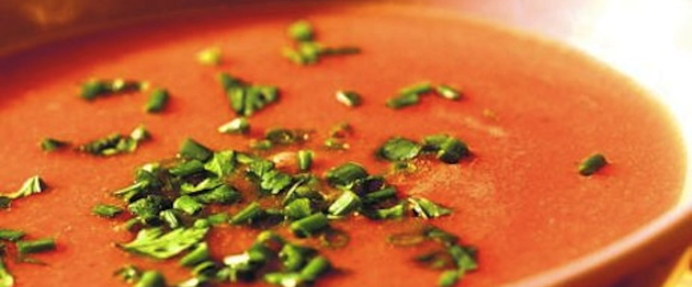 Rød suppe i skål, med grønt strødd oppå.